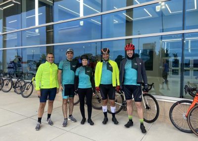 Bluebonnet express biking team group photo outside modern glass building.
