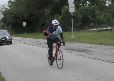Cyclist riding along rural road with traffic signs, promoting Bluebonnet Express cycling events.