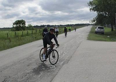 Cyclists enjoying a ride on a scenic outdoor road with cloudy sky and green landscape.