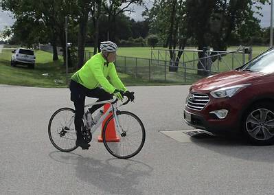 Bike rider in neon jacket riding along city street near cars and trees.
