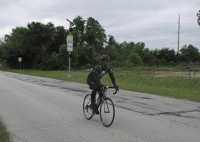 Cyclist riding along the road on a Bluebonnet Express bike route with greenery and road signs in the background.