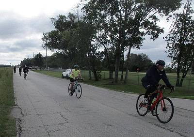 Bike riders enjoying a scenic ride on a cloudy day along a quiet, tree-lined street.