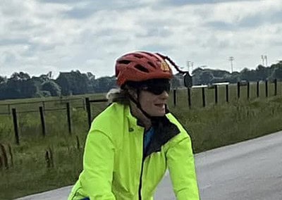 Bright yellow cycling jacket on woman riding a bike on rural road during cloudy day.