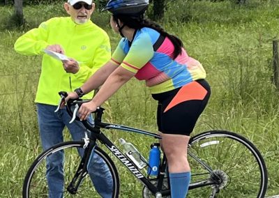 Young woman in colorful cycling attire on a road bike, consulting with an older man during a ride.