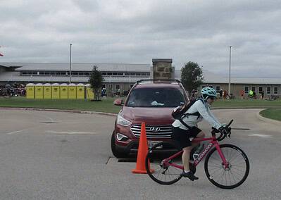 Vibrant cyclist riding past Hyundai vehicle at Bluebonnet Express event in Texas outdoor setting.