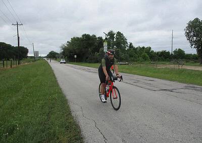 Bright cyclist riding on rural road with greenery and overcast sky - Bluebonnet Express cycling route.