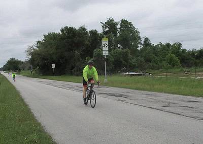 Cyclist in neon jacket riding on rural road with speed limit and safety signs, scenic outdoor biking route.