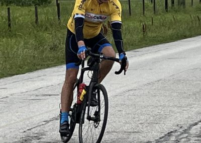 Vastly, a cyclist riding on a rural road in a yellow Colombia cycling jersey and black helmet.