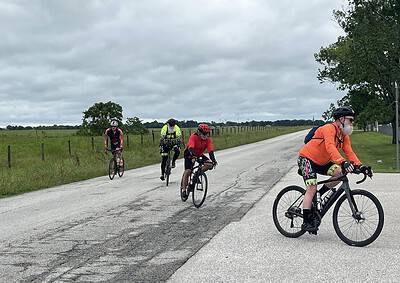 Cyclists riding on a scenic rural road during daytime with overcast sky.