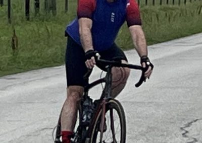 Man cycling on a rural road with a blue and red cycling jersey and helmet.