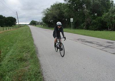 Cyclist riding on the rural road with green trees and overcast sky, promoting Bluebonnet Express biking services.