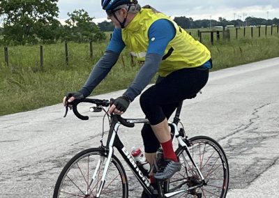 Bright yellow cycling vest, riding a Trek road bike on a rural road, with a scenic green field background.