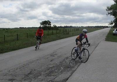 Bicycle riders on road with cloudy sky, highlighting Bluebonnet Express bike route.