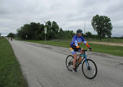 Bright blue and orange cyclist riding along rural road during Bluebonnet Express event, promoting outdoor biking.