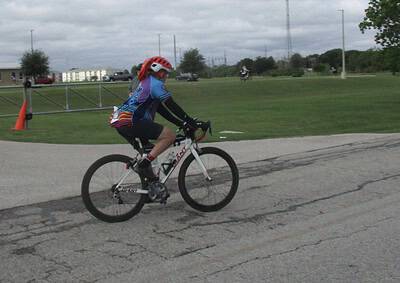 Vibrant cyclist wearing a blue jersey and red helmet riding a mountain bike on a paved trail at Bluebonnet Express event.