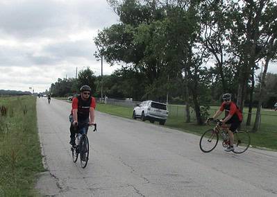 Cyclists riding along a rural road on a cloudy day, promoting outdoor biking with Bluebonnet Express.