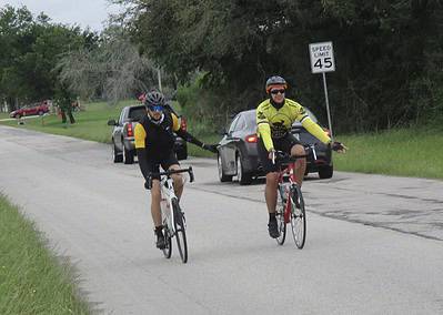 Cyclists riding on a suburban road near cars, promoting safe biking in Bluebonnet Express.