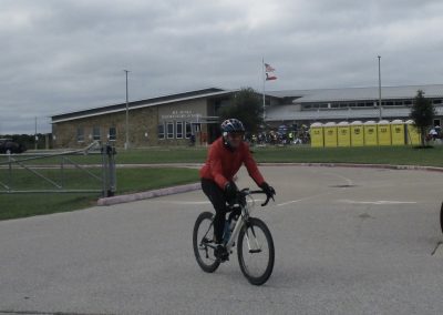 Bright red jacket cyclist riding near elementary school, Bluebonnet Express, Texas bike delivery.