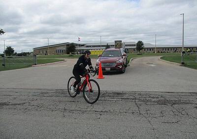 Cyclist riding a bike at Bluebonnet Express, Texas bike trail with school in background.