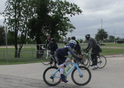 Bicycle riders participating in a cycling event along a park path on a cloudy day.