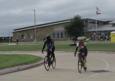 Bike riders at Bluebonnet Express event outside elementary school during daytime, showcasing cycling community.