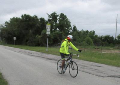 Cyclist riding on rural road with safety gear and bright yellow jacket, promoting bike safety and outdoor activity.