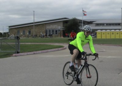 High-visibility cyclist riding outside Bluebonnet Express bike station with Texas flags in background.