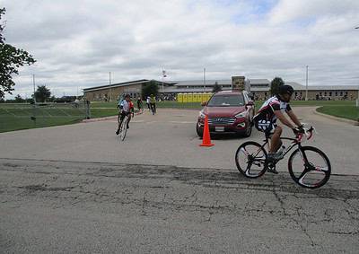 Cyclists riding near Bluebonnet Express school, with a red Hyundai SUV and orange traffic cone in the background.