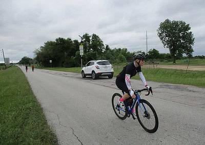 Bike rider on scenic rural bike trail with cars and trees, promoting Bluebonnet Express cycling events.