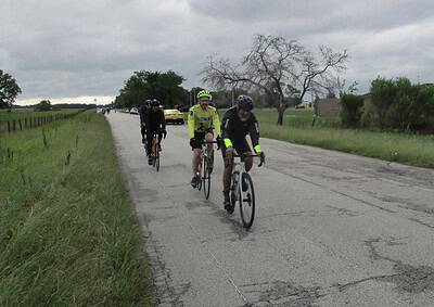 Group of cyclists riding on a rural road during overcast weather, promoting Bluebonnet Express cycling event.