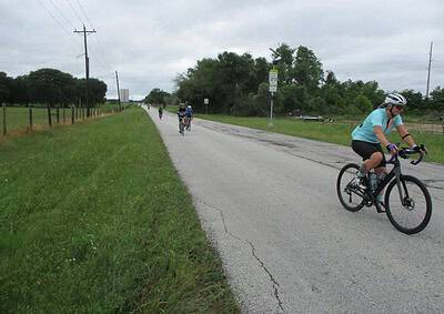 Cyclists riding along a rural road during daytime under cloudy sky, promoting outdoor biking.