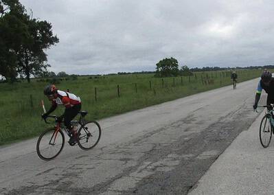 Severe bike lane damage on rural road with cyclists riding safety near the Bluebonnet Express.