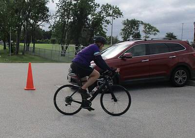 Rider on a mountain bike crossing the street near a parked red car.