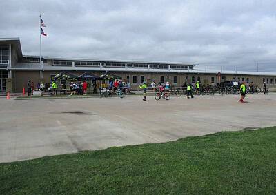 Cyclists gather outside a community center for Bluebonnet Express bike event under cloudy skies.