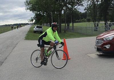 Bright neon cyclist participating in Bluebonnet Express bike race near park and cars.