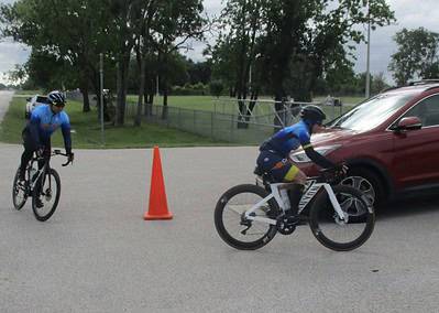 Cyclists participating in Bluebonnet Express bike race near a red car on a cloudy day.