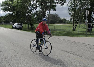 Cyclist wearing red jacket and blue helmet riding a bike on a suburban street.