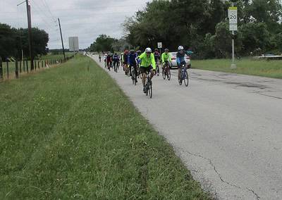 Group of cyclists riding along rural roadway on Bluebonnet Express route, outdoor biking adventure.