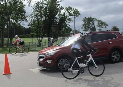 Bicycle and car safety at Bluebonnet Express event, cyclist passes parked vehicle on street.