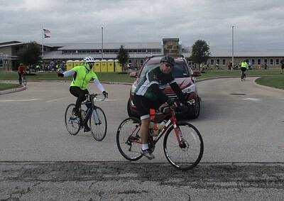 Riders in high-visibility gear participating in Bluebonnet Express bike event, cycling past school grounds on a cloudy day.