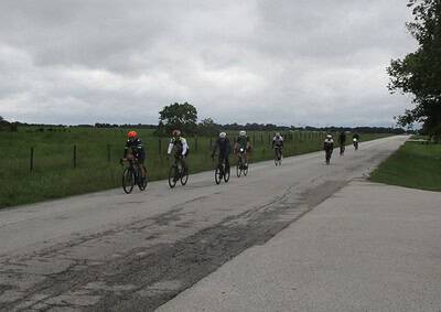 Cyclists riding on rural Texas road with overcast sky, part of Bluebonnet Express bike route.
