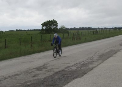 Cyclist riding on rural road in green countryside during overcast weather.