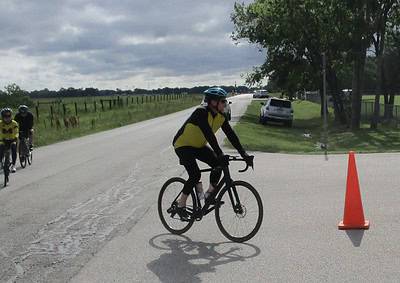 Cyclist riding past traffic cone on a suburban road during a cycling event or training.