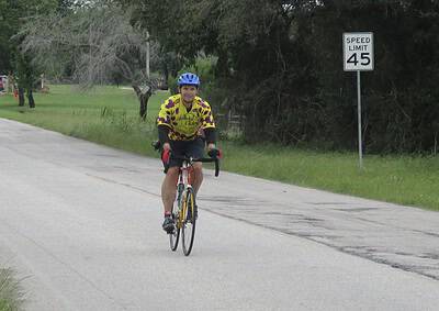 Cyclist riding on rural road, wearing Bluebonnet Express cycling jersey and helmet for safety.