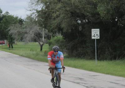 Bright cyclist on Texas road with Bluebonnet Express branding and speed limit sign in the background.