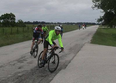 Group of cyclists riding on a rural road during daytime, engaging in outdoor biking activities.
