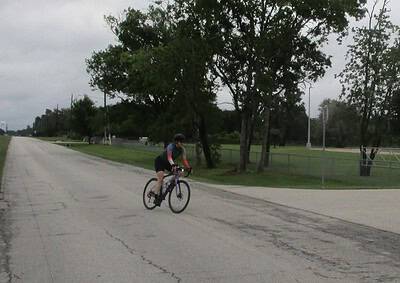 Cyclist riding on a road with trees and overcast sky, promoting Bluebonnet Express bike services.