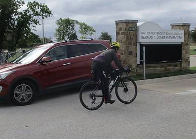 Cyclist riding a bike past a school entrance in cloudy weather, emphasizing transportation and local school commute.