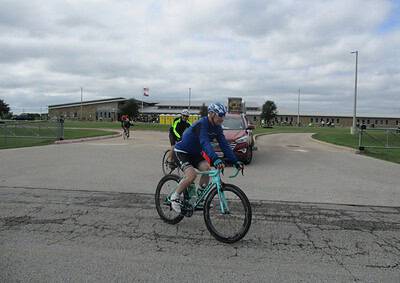 Bike ride at Bluebonnet Express event with cyclists and supporters outside a community center under cloudy skies.