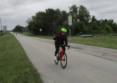 Bright green helmet cyclist riding on bike path near trees - Bluebonnet Express biking trail.